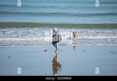 femme d'âge moyen ou plus âgée promenant son grand chien de compagnie le long d'une plage sur le sable humide à marée basse. Chien de promenade femelle sur la plage vide île de wight. Banque D'Images