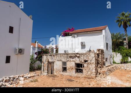 Scène de rue méditerranéenne lumineuse avec des maisons en plâtre blanc, une ruine en pierre altérée, des palmiers et un ciel bleu clair. Kalkan, Turquie Banque D'Images