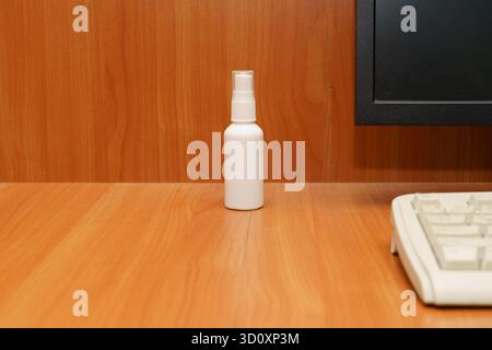 Un vaporisateur blanc propre se trouve sur un bureau en bois à côté d'un écran d'ordinateur et d'un clavier dans un espace de travail bien rangé. Banque D'Images