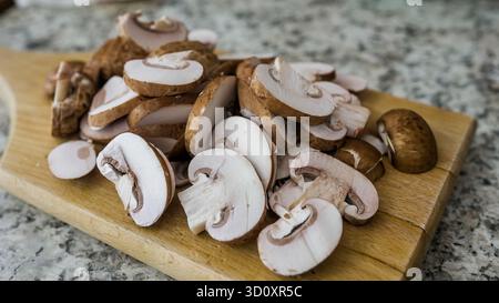 Les champignons sont soigneusement tranchés et disposés sur une planche à découper en bois clair. Le cadre de la cuisine est lumineux, mettant en valeur les produits frais. Parfait pour un Banque D'Images