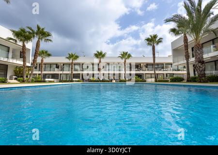 Grande piscine extérieure dans un complexe d'appartements moderne avec des palmiers, entouré de bâtiments blancs et ciel nuageux. Banque D'Images