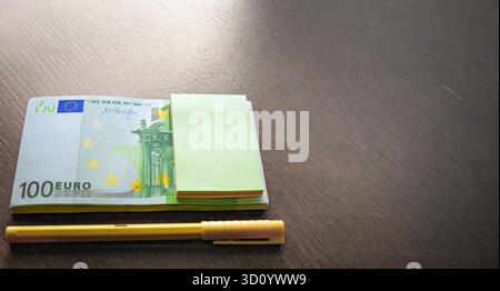 Cent billets en euros avec stylo jaune et bloc-notes sur fond en bois Banque D'Images