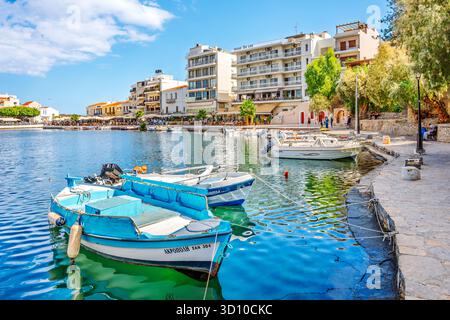 Bateaux de pêche le long de la promenade du front de mer avec des cafés de trottoir au loin sur le lac Voulismeni dans la pittoresque ville balnéaire d'Agios Nikolaos. Banque D'Images