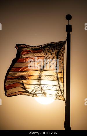 Drapeau américain au coucher du soleil Washington DC // WASHINGTON DC — un drapeau américain flotte au coucher du soleil près du Washington Monument. Le drapeau, emblème national des États-Unis, comporte 13 bandes horizontales et 50 étoiles blanches sur un canton bleu. Les rayures représentent les treize colonies originales, tandis que les étoiles symbolisent les 50 états. Le Washington Monument est un obélisque important sur le National Mall, honorant George Washington, et Washington D.C. est la capitale des États-Unis. Banque D'Images