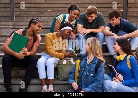 Groupe d'étudiants diversifié interagissant, partageant un smartphone dans les escaliers Banque D'Images