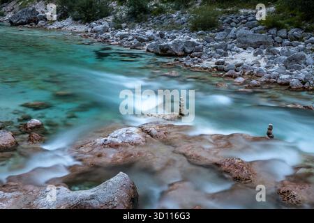 La rivière Soca coule parmi les rochers à Bovec, Slowenia. Des arbres se dressent près de la rivière et des piles de pierre s'élèvent de l'eau. Banque D'Images