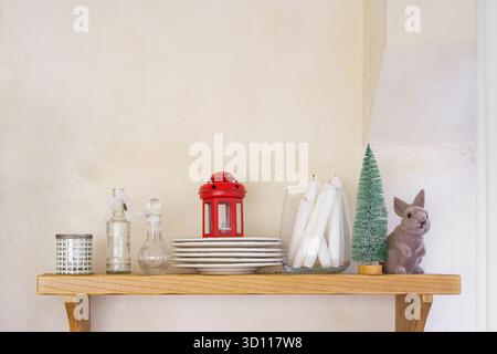 Étagère en bois décorée de bougies blanches, d'une lanterne rouge, de bouteilles en verre, d'un lapin en céramique et d'un petit sapin de Noël. Intérieur confortable maison de vacances rustique wi Banque D'Images