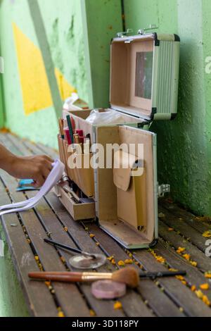 Maquilleuse professionnelle ouvrant un étui de beauté portable avec des pinceaux et divers produits cosmétiques sur un banc en bois Banque D'Images