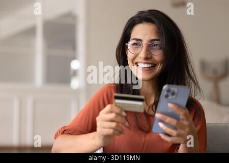 Heureux client de banque latine femme dans des lunettes en utilisant la carte de crédit Banque D'Images