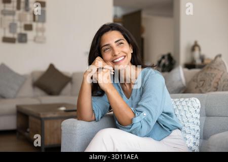 Joyeuse belle jeune femme hispanique assise sur un canapé confortable Banque D'Images