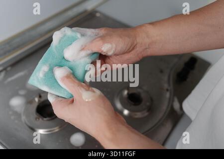 Travailleur de l'entreprise de nettoyage pressant l'eau savonneuse de l'éponge pendant le nettoyage du poêle à gaz sale, pour enlever la saleté, la graisse, la promotion de l'hygiène, la propreté Banque D'Images