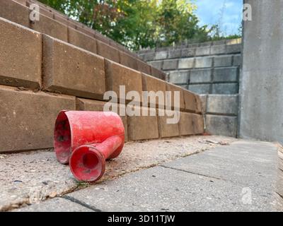 Un arrosoir rouge est abandonné sur des marches en béton à l'extérieur. Symbole pour les souvenirs d'enfance perdus solitude urbaine et le passage du temps dans Everyda Banque D'Images
