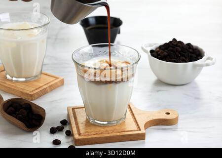 Verser une dose de café noir dans le verre avec du lait frais froid. Processus de préparation d'une tasse crémeuse Latte Coffee sale Banque D'Images
