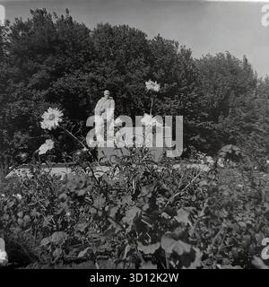 Le complexe commémoratif de la seconde Guerre mondiale avec une flamme éternelle à la KhimProm (usine chimique) à Sloviansk, dans les années 1970 Cette photo d'archives en noir et blanc de l'URSS, la RSS d'Ukraine, montre le monument de l'usine dédié à la Grande Guerre patriotique. Le mémorial présente une statue d'un soldat soviétique dans un imperméable debout sur un piédestal, avec des plaques commémoratives derrière lui. Un brûleur à flamme éternelle (non allumé) est à l'avant. Le monument est entouré d'un parterre de fleurs. Cette image capture un mémorial de guerre soviétique typique dans une entreprise industrielle. Un document de vie paisible dans le Donbass avant la guerre. Banque D'Images