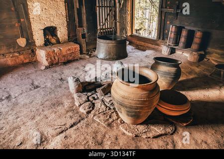 7 septembre 2025, Sirogojno, Serbie : salle rustique avec sol en terre, avec des pots en argile, un foyer de cuisson et des tonneaux en bois Banque D'Images
