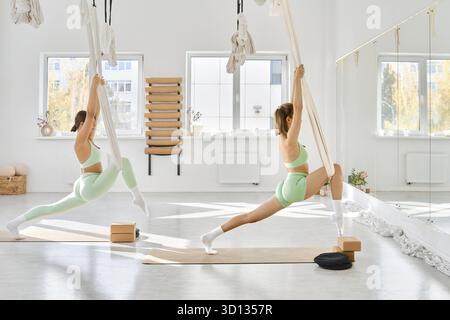 Dans un studio de fitness spacieux rempli de lumière naturelle, deux individus s'engagent dans des exercices d'étirement avec des hamacs Banque D'Images