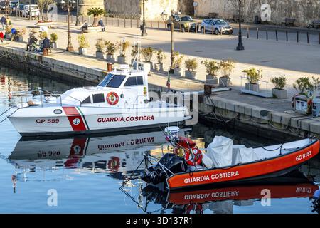 Alghero, Sardaigne - Italie - 2025 : deux patrouilleurs Guardia Costiera réfléchissent sur l'eau calme près d'un quai. Un bateau blanc et un bateau rouge se détachent près d'un coa Banque D'Images