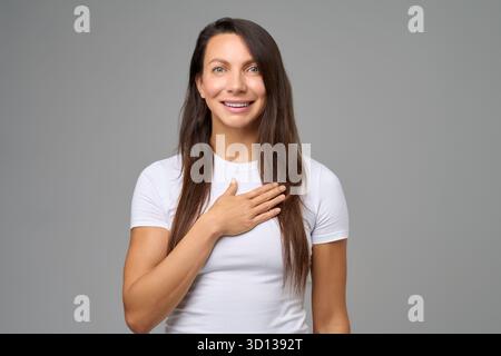 Femme souriant d'une main sur la poitrine exprimant la sincérité et l'émotion positive Banque D'Images