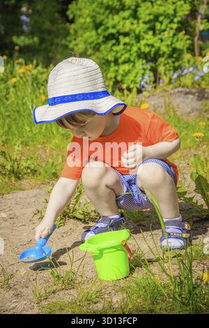 Un garçon avec un seau et une pelle jouant dans le sable. Jeux pour enfants. Été et sable. Le garçon a une photo brillante. Le garçon joue une photo brillante Banque D'Images