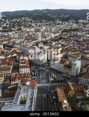 Vue aérienne des toits en terre cuite embrassés par le soleil qui s'étendent à travers le paysage urbain, juxtaposés contre les collines verdoyantes en arrière-plan, Trieste, Frioul-Vénétie Julienne, Italie. Banque D'Images