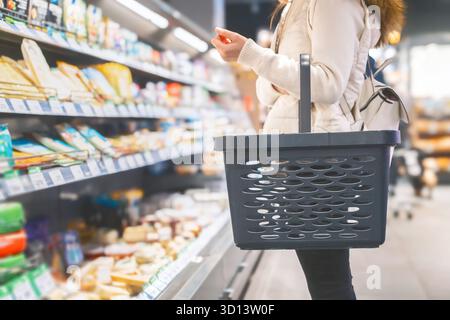 Une femme se tient debout dans une allée d'épicerie, tenant un panier noir. Elle sélectionne soigneusement les produits des étagères remplies de divers Banque D'Images