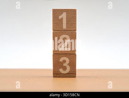 Trois blocs de bois sont empilés les uns sur les autres, chacun affichant un nombre de un à trois. Le réglage est simple et met en évidence le nat des blocs Banque D'Images