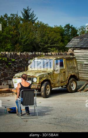 Un artiste assis en train de peindre et une vieille camionnette en décomposition dans un cadre rural Banque D'Images