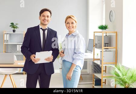 Deux collègues, homme et femme sourient tout en se tenant debout dans l'espace de bureau du centre d'affaires. Banque D'Images