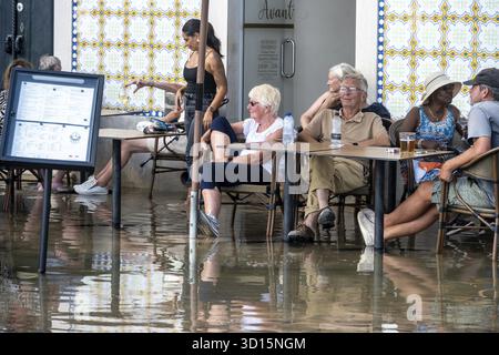 Tavira, Algarve - Portugal - 09-18-2024 : les gens dans un café en plein air inondé sous des parasols, en profitant de boissons, avec façade de bâtiment carrelée Banque D'Images