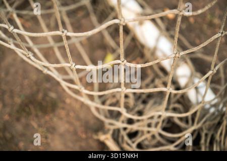 Gros plan d'un vieux filet de but de football usé montrant des fibres effilochées et une texture altérée. Mise au point sélective. Banque D'Images