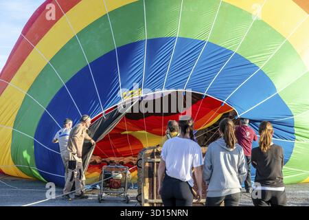 Guadix, Grenade - Espagne - 2024 : enveloppe colorée en montgolfière aux couleurs de l'arc-en-ciel, partiellement gonflée, avec des personnes impliquées dans la configuration et la préparation Banque D'Images