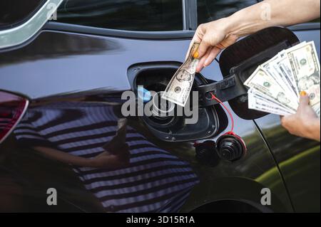 Main de femme qui met de l'argent dans le réservoir de voiture, gros plan, concept de carburant cher, crise de carburant Banque D'Images