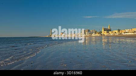 Plage de Regla avec église et phare à Chipiona dans la lumière chaude du soir Banque D'Images