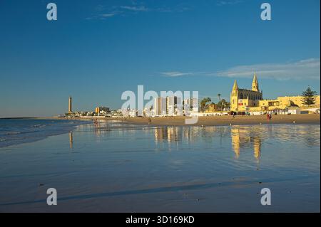 Plage de Regla avec église et phare à Chipiona dans la lumière chaude du soir Banque D'Images