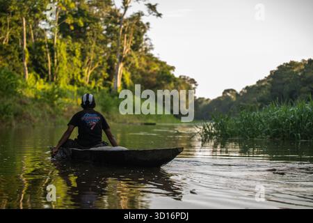 Homme pagayant un canoë en bois le long d'une rivière calme au coucher du soleil dans la forêt amazonienne près de Nauta, Loreto, Pérou, 2024. Banque D'Images