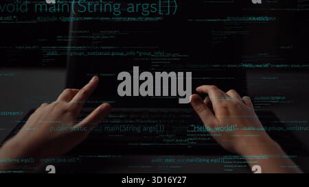 Les mains sont vues taper sur un ordinateur portable dans un environnement sombre, avec des lignes de code affichées sur l'écran. Cette image capture l'essence de la programmation d'un Banque D'Images