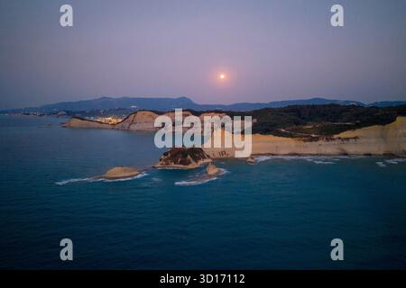 Large panorama aérien de la pleine lune se levant au-dessus du cap Drastis, Corfou, Grèce. Les falaises blanches et le littoral sont illuminés par le crépuscule et lointain Banque D'Images