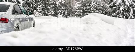 Voiture argentée couverte de glace garée sur une route recouverte de neige profonde, vue de détail de derrière, arrière-plan d'arbres flous espace vide pour le texte côté droit Banque D'Images