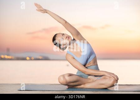 Heureuse jeune femme expérimentée professeur de fitness effectue le yoga parshvottanasana assis sur la plage le matin Banque D'Images