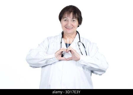 Femme médecin portant un manteau blanc et un stéthoscope, souriant à la caméra et formant une forme de coeur avec ses mains, symbolisant le soin, l'amour Banque D'Images