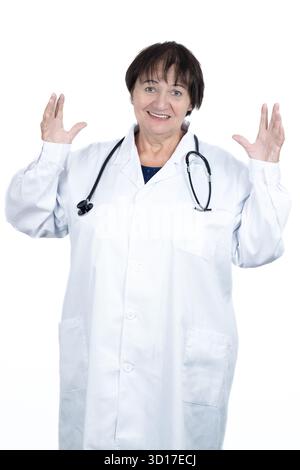 Médecin senior femme portant une blouse de laboratoire blanche et stéthoscope, souriant tout en faisant des gestes avec confiance avec les deux mains vers le haut, montrant l'expertise médicale et co Banque D'Images