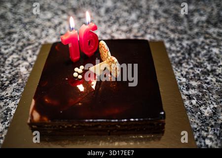 gros plan d'un délicieux gâteau d'anniversaire au chocolat noir avec une bougie célébrant 16 ans, décorée de deux barres de chocolat blanc Banque D'Images