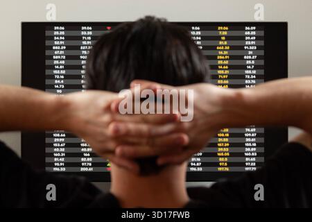 Gros plan sur l'arrière d'un homme dans l'attitude relaxante regardant un écran avec des valeurs boursières Banque D'Images