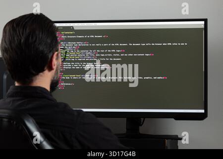 Gros plan sur un homme en arrière sur le côté gauche de l'image regardant un écran d'ordinateur avec un programme d'écriture de code html Banque D'Images