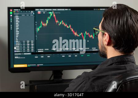 Gros plan sur un homme en arrière sur le côté droit de l'image regardant un écran d'ordinateur avec un plattform de marché boursier Banque D'Images
