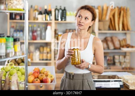 Femme shopper choisissant soigneusement le pot d'olives en conserve dans le supermarché d'épicerie Banque D'Images