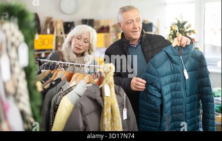 Couple âgé debout dans le magasin de Noël et choisissant des vestes Banque D'Images