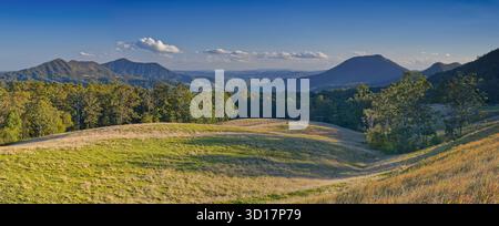Admirez les sommets de la vallée de Lynch's Creek au premier plan des prairies ensoleillées tôt le matin et le ciel bleu du parc national Border Ranges, en Nouvelle-Galles du Sud, Australie Banque D'Images