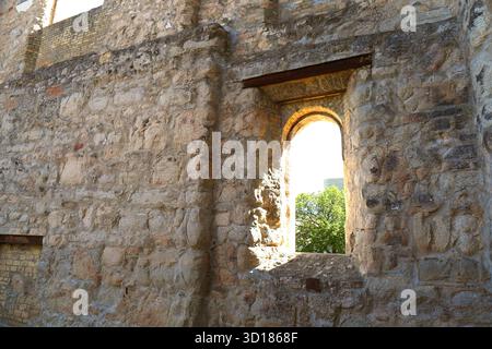 Vieux mur de pierre avec fenêtre cintrée.la lumière du soleil brille à travers une fenêtre cintrée dans un vieux mur de pierre de ruines historiques, créant un atmo chaleureux et nostalgique Banque D'Images