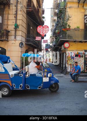 Taxi bleu à trois roues dans une rue animée avec des décorations suspendues à Palerme Sicile Banque D'Images
